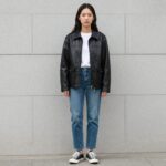 검정 가죽 라이더 자켓을 입은 여성이 청바지와 스니커즈와 함께 캐주얼하게 코디한 모습
