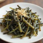 완성된 곰취나물 무침이 접시에 담겨 있으며, 들기름과 통깨가 뿌려져 있다.