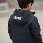 내셔널지오그래픽 카본블랙 키즈 바람막이 점퍼를 입은 아이 뒷모습, 3M 반사 로고 테이프가 보임