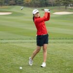 와이드앵글 레드 컬러 피크닉 아노락을 입은 모델이 골프 필드에서 포즈를 취하고 있다