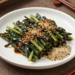 데치고 양념한 오가피순나물무침이 접시에 담겨 있고 옆에 통깨가 뿌려져 있다